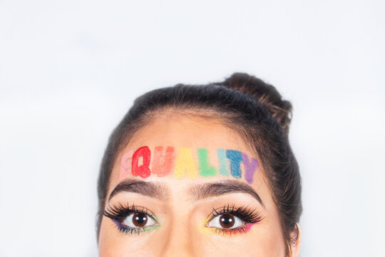 Phrase 'equality' written on the forehead of a beautiful young girl in gay pride makeup, with copy space.