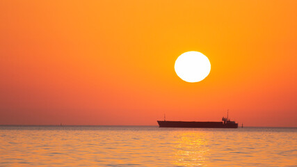 orange sunrise at sea with the silhouette of the container ship