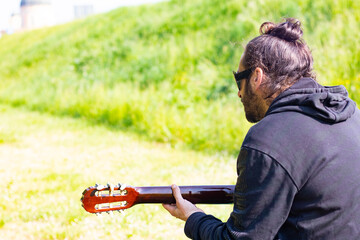 Hippy man with beard and glasses playing guitar outdoors on the grass