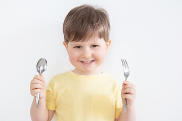 Happy boy holding a spoon and a fork