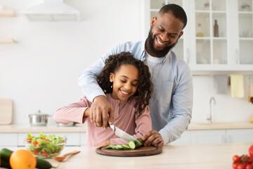 African american father teaching daughter how to prepare salad