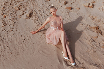 Beautiful blonde woman posing in embroidery dress on desert, lying on sand, at the sunset light.