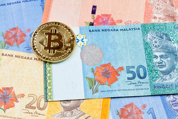 Close-up on a golden Bitcoin coin on top of a stack of Malaysian Ringgit banknotes.