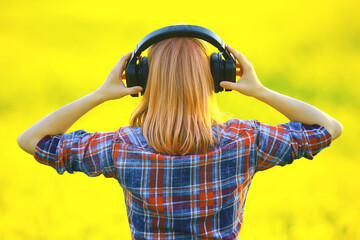 back view of a girl in headphones listening to music in a field of flowers, springtime music is happy