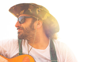 Hippy man with hat beard and glasses playing guitar outdoors on the beach