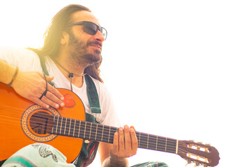Hippy man with beard and glasses playing guitar outdoors on the beach