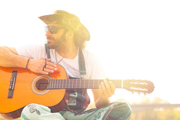 Hippy man with hat beard and glasses playing guitar outdoors on the beach