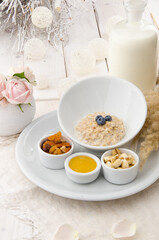 Oatmeal with blueberries in a beautiful white plate with honey, berries and a banana on a light delicate background. Healthy breakfast.