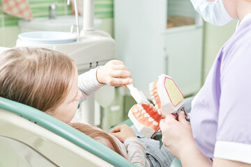 Dentist teaching girl how to brush teeth. Pediatric dentist educating a child about tooth-brushing on a model.