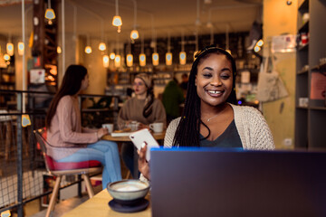 Portrait of young woman working on using laptop at coffee shop.