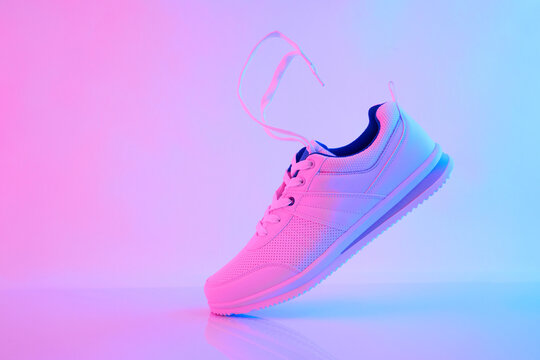 Hand Hold White Sneakers With Flying Laces In Neon Light. Sport Shoes For Training In The Gym. Creative Minimalism. 90s Concept.