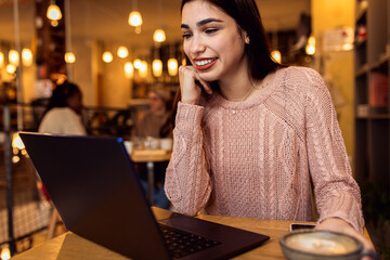 Portrait of young woman working on using laptop at coffee shop.