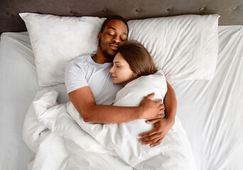Top view of affectionate multiracial couple hugging each other while sleeping in bed
