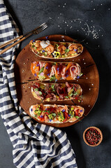 Italian Bruschetta antipasto - Grilled Bread topped with tomato, vegetables, cured meat, salted fish. Various bruschetta on dark textured table top view. Food flat lay, italian rustic dish concept.