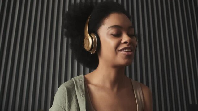 The portrait of a smiling black woman listening music with headphones in the room