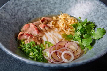Vietnamese Cuisine - Beef Pho Noodle Soup or Pho Bo Soup. Served with Fresh Greens in Blue Bowl on...