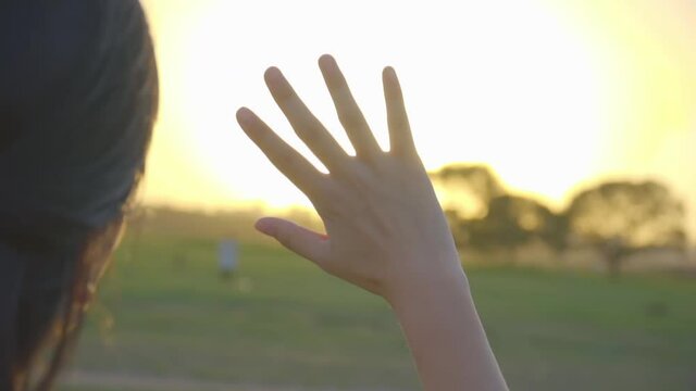 A girl shielding her eyes from sunlight to see field scenery at sunset
