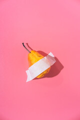 A ripe pear is glued with white tape to a pink background. Creative fun concept in the style of minimalism.