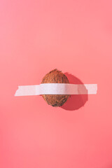 The coconut is glued with white tape to a pink background. Creative fun concept in the style of minimalism.