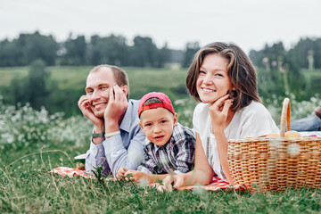 Happy family resting in nature. Mother, father and child Enjoying and lying on checkered plaid in meadow