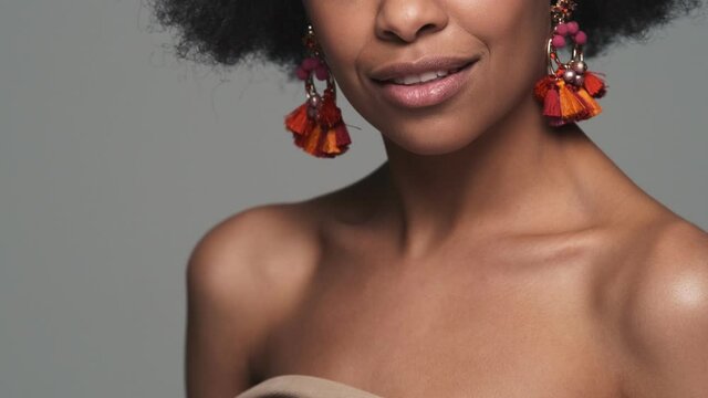 The close-up view of the collarbones of a black smiling woman with earrings in the studio