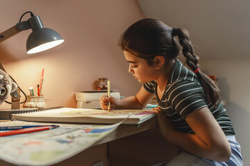 Little girl practising and learning to draw.She sitting at the table in her room.
