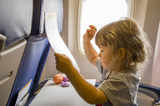 Portrait of a little girl in the cabin of the plane near the window, looking at the pictures of the magazine.