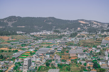 Panorama landscape, Dalat city, Langbian Plateau, Vietnam Central Highland region. Vegetable fields, many houses, architecture, farmlands, greenhouse. Mountain background. Green Gray smoky toned photo