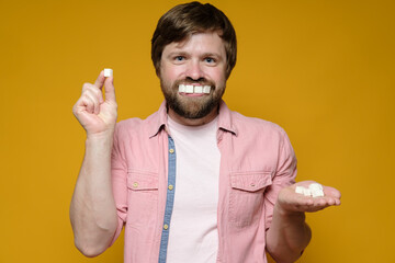 Funny man put sugar lumps in mouth as if it were teeth and smiles. Yellow background.