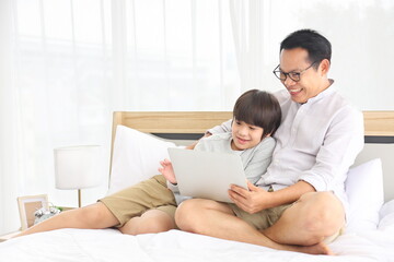 Asian father teaching homework to his son in bed for homeschooling and education concept