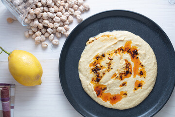 Home made hummus bowl, decorated with boiled chickpeas, lemon and olive oil over a rustic white background.