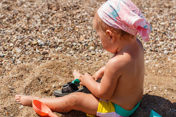 Tanned baby girl in swimsuit sits on the sand in summer