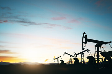 Oil production concept with oli pumps silhouettes outdoors at sunset on blue sky background