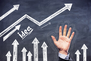 Man hand rised near the arrows headed up and idea word on a blackboard background. Creativity and...
