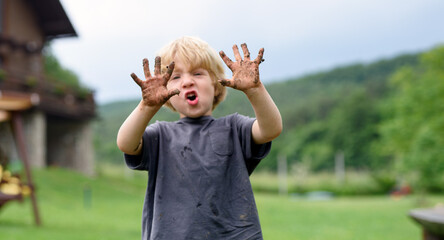 Small boy with dirty hands standing in vegetable garden, sustainable lifestyle.