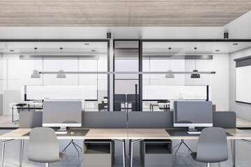 Modern light coworking office design with glass partitions, desks with computers, white walls and concrete floor