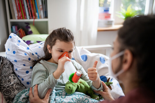 Mother and sick small daughter using inhaler in bed at home, coronavirus concept.