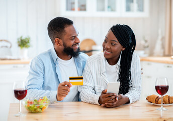 Black Couple Ordering Food Online With Smartphone And Credit Card In Kitchen