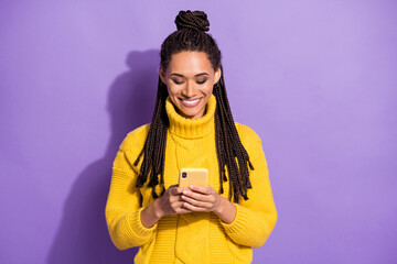 Photo portrait of smiling girl texting holding phone in two hands isolated on vivid purple colored background