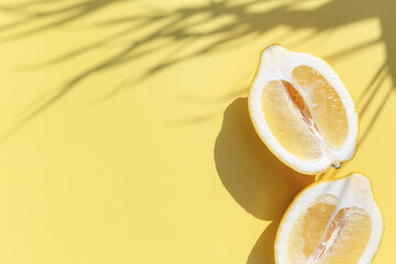Two halved cuts of lemon with shadow from palm leaf on yellow background