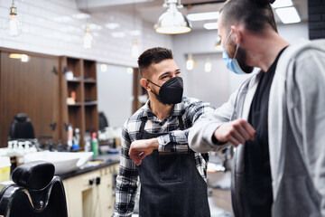 Man greeting haidresser with elbow bump in barber shop, coronavirus and new normal concept.