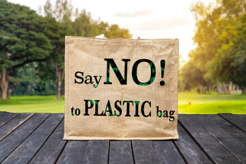 Jute bag with say No to plastic bag logo hanging on old wooden wall with blurred nature background, ecological object concept