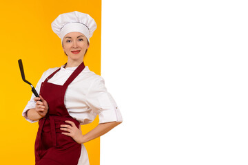 Сook next to a white poster. Woman in chef uniform. Girl cook on a yellow background. Concept - place for an inscription about preparation of dishes. Restaurant chef career. Cooking training
