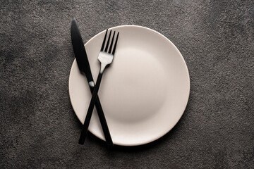 a white empty plate on a gray background and a fork and knife. Concept for a restaurant or menu