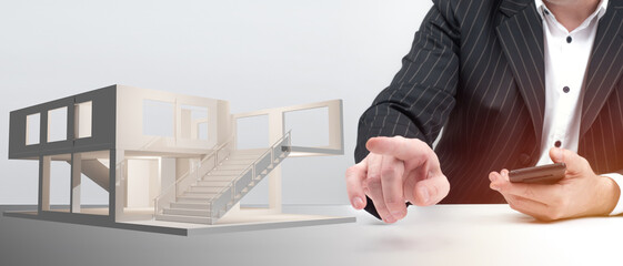 Businessman next to architectural model. Concept - construction of commercial real estate. Architectural design of business center. A man in a business suit points to layout of house.