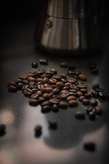 Roasted coffee beans of different kinds on gray surface and an Italian coffee pot in the background.