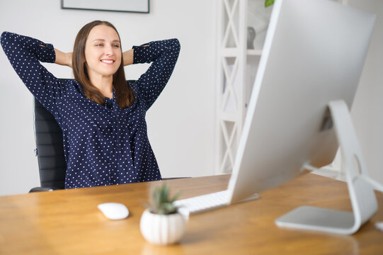 Smiling Female Employee Takes A Break On The Workplace In The Office, Leaned Back In The Chair Rests With Satisfied Face Expression, Woman Rejoices With Finished Project Or Workday Over