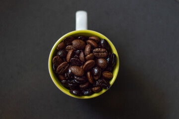 Cup of coffee with roasted coffee beans inside of different shades and kinds on a gray background. Coffee beans surrounding mug. Copy space