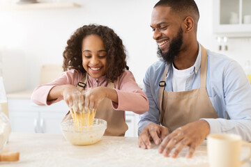 Happy afro dad and daughter mixing dough together in kitchen