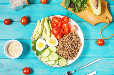 Vegan lunch bowl with avocado, egg, cucumber, tomato and buckwheat on blue wooden background